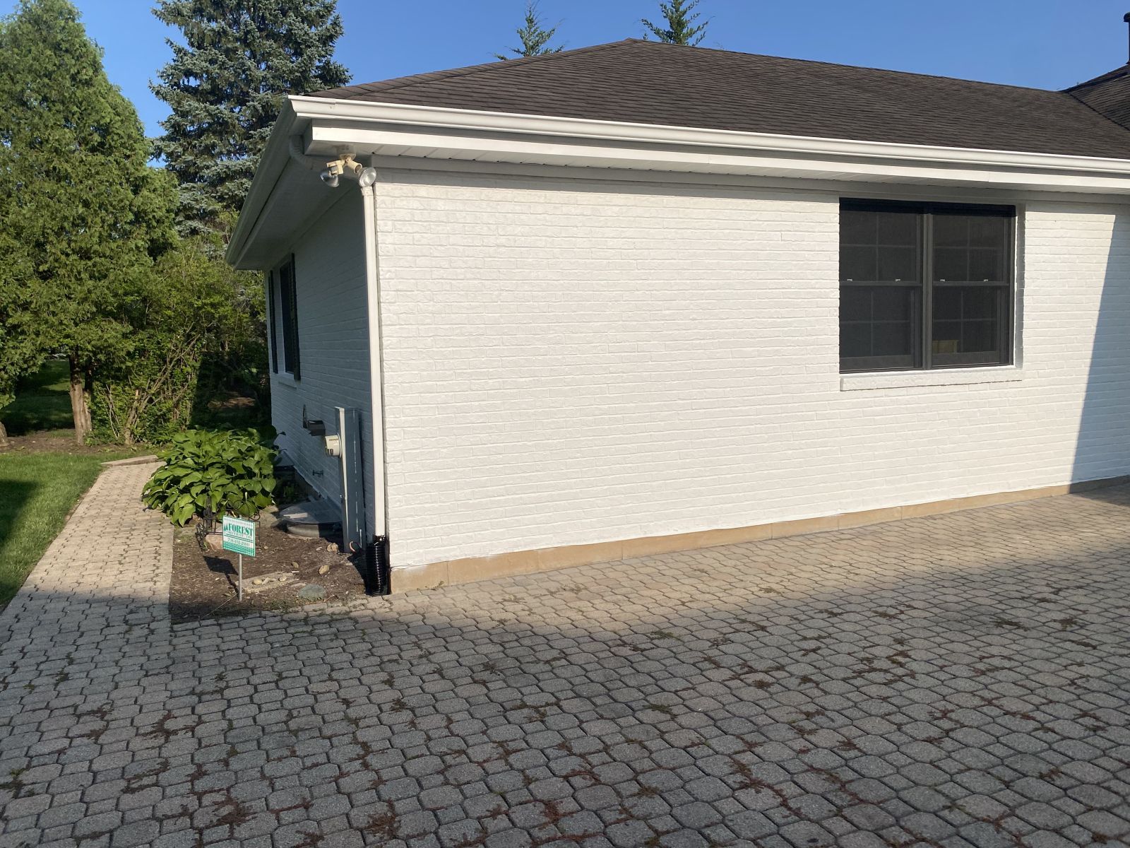 White house exterior with dark roof, driveway pavers, and trees beside it