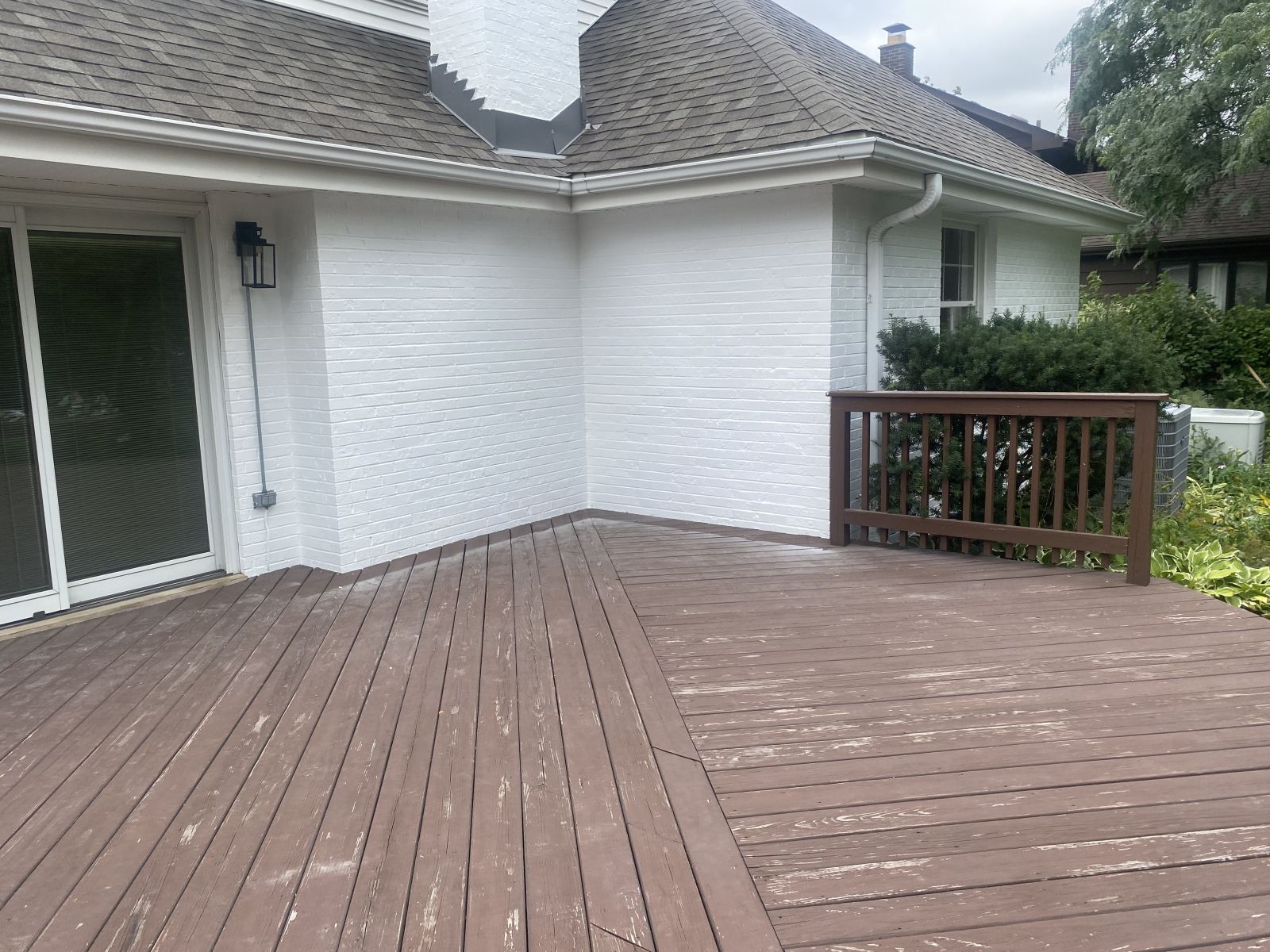 Wooden deck beside a white house with sliding glass door and railing overlooking a yard.
