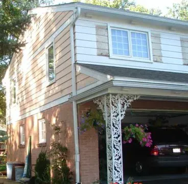 Two-story brick-and-siding house with an open garage and decorative white porch trim.
