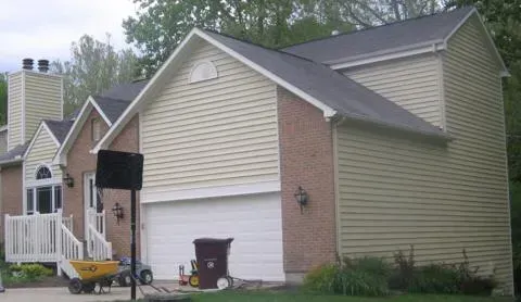 Suburban house exterior with white garage, beige siding, and a front porch by trees