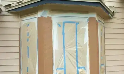 House exterior windows and siding masked with blue painter’s tape and paper for painting