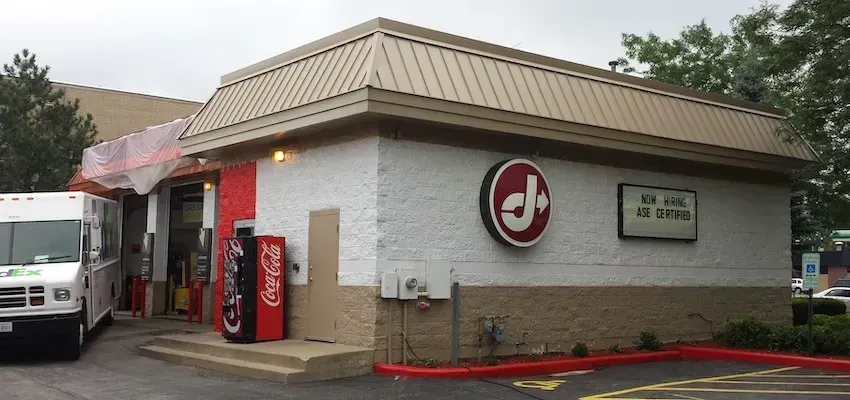 Drive-thru restaurant corner with red logo sign, soda machine, and parked truck