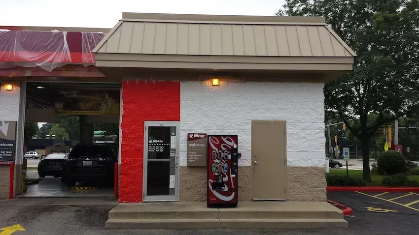 Small building exterior with a red brick wall, vending machines, and a covered drive-through area