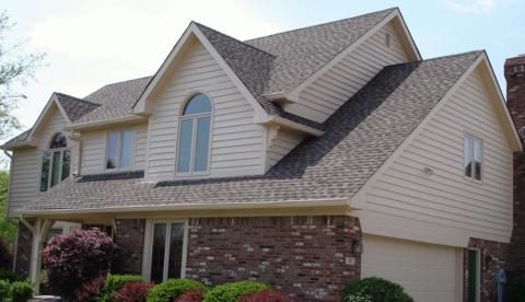 Suburban two-story house with beige siding, brick lower facade, and a gray shingled roof