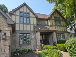 Tudor-style brick-and-stucco house with gabled windows, front entry, and manicured shrubs