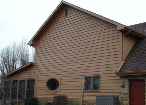 Tan house siding with round window and red door on a cloudy day