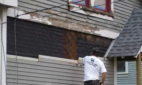 Worker repairing the exterior wall of a house with siding removed and exposed framing