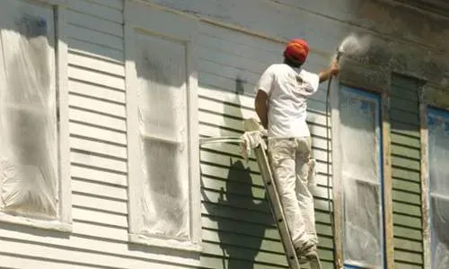 Worker painting the exterior of a white house while standing on a ladder