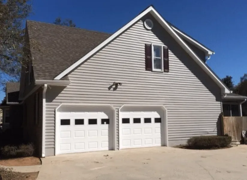 Gray house exterior with two white garage doors and dormer windows under a blue sky