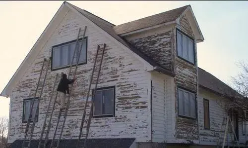 Old weathered house with peeling white paint and ladders leaning against the front wall.