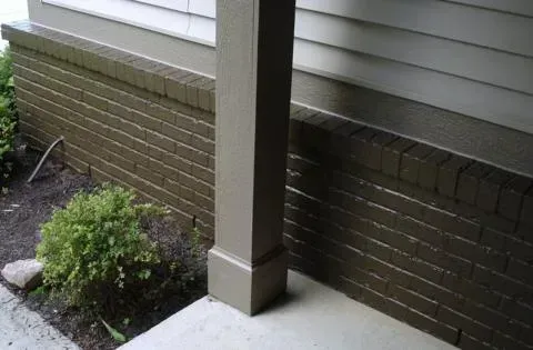 Brick house exterior with a porch post, concrete stoop, and small shrub by the wall.