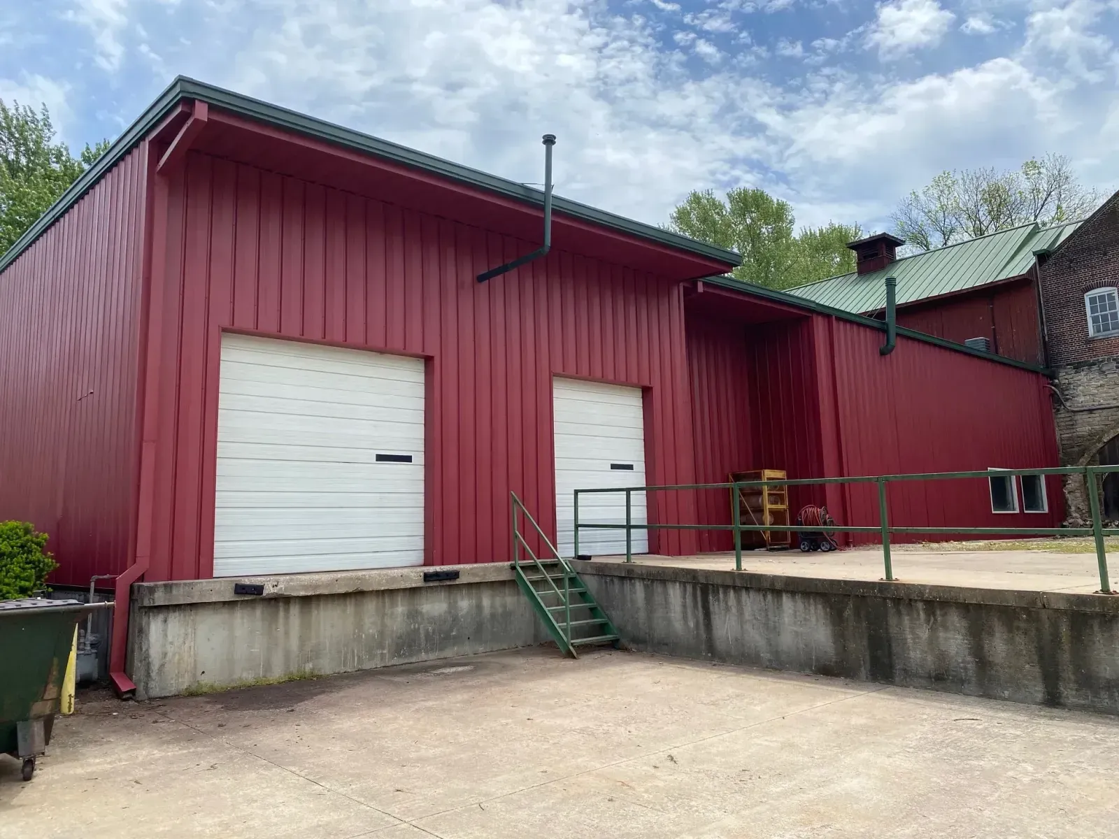 Red warehouse loading dock with white doors, green stairs, and a concrete ramp