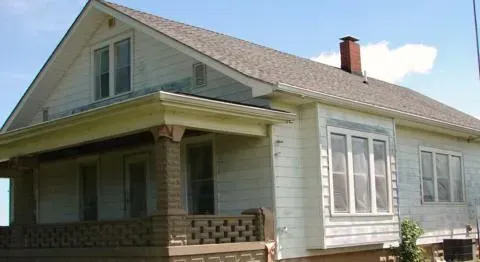 Small white house with a front porch and gabled roof in daylight