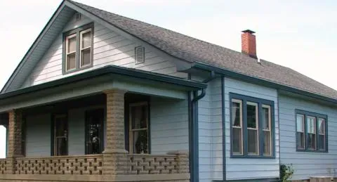 Blue-gray house with a porch, gabled roof, and red chimney on a cloudy day