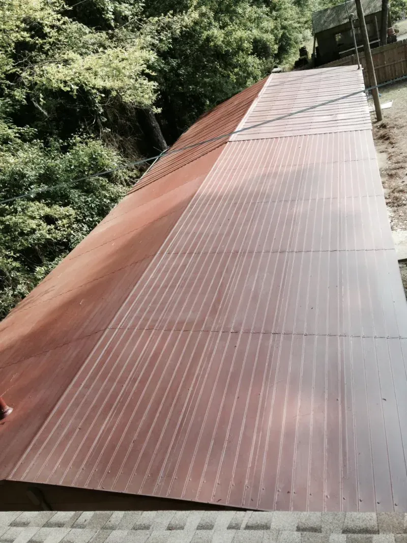 Corrugated rust-red roof on a building beside dense green trees