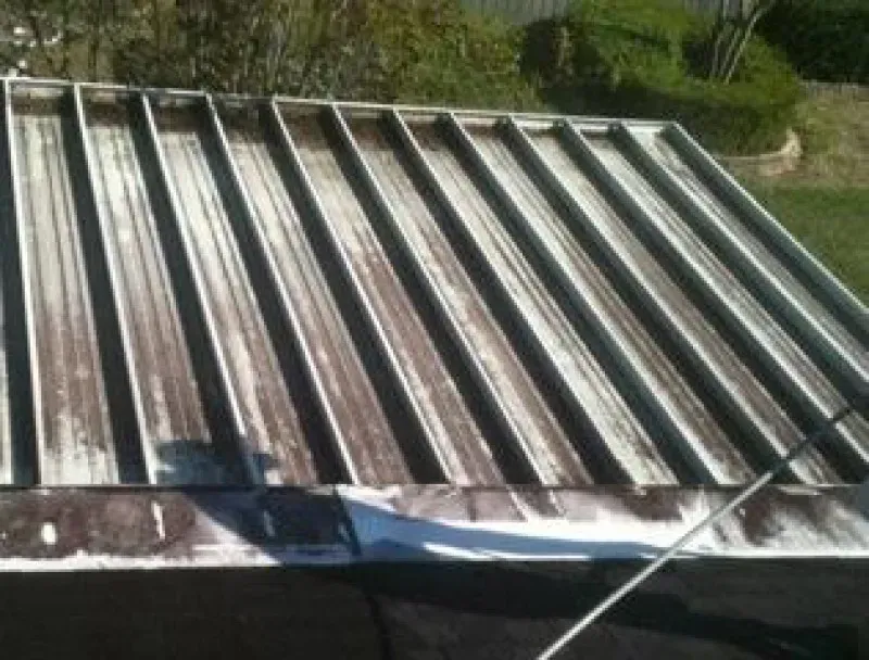 Metal roof panels lying on the ground outdoors, with grass and a garden in the background