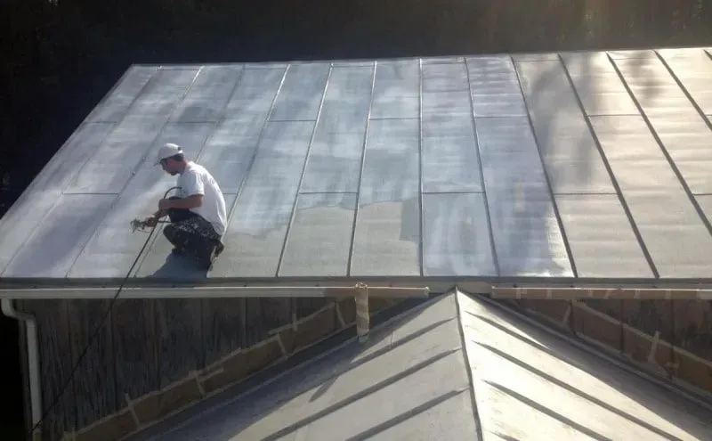 Worker on a sloped metal roof, using a safety harness and rope.