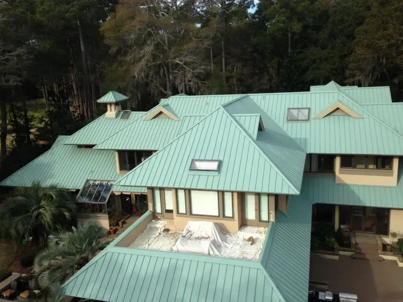 Large house with a teal metal roof nestled in trees and greenery