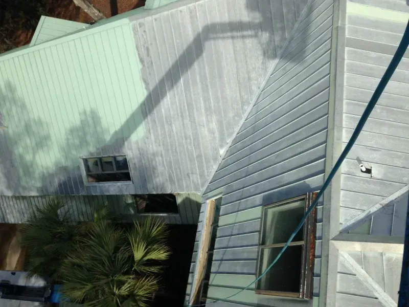 Aerial view of a house roof with solar panels, white siding, and palm trees below.