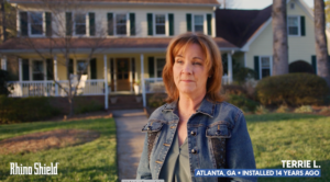 Woman stands in front of a large suburban house on a sunny day.