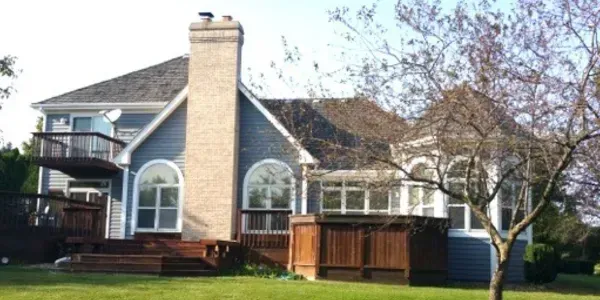 Suburban house with blue siding, a tall brick chimney, arched windows, and a wooden fence in front