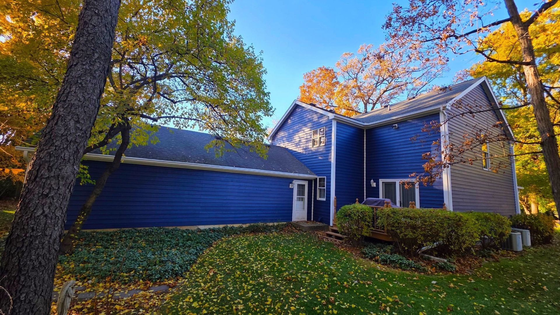 Blue house with autumn trees and fallen leaves, viewed from the front yard