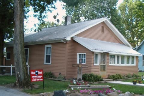 Small brown house with white trim and a red sign in the front yard
