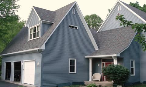 Blue-gray house with steep gables, white trim, and a small front porch surrounded by greenery