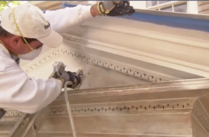 Worker cleaning ornate ceiling molding with a long hose and power tool