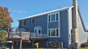 Blue two-story house with a wooden deck and white-trimmed windows under a clear sky