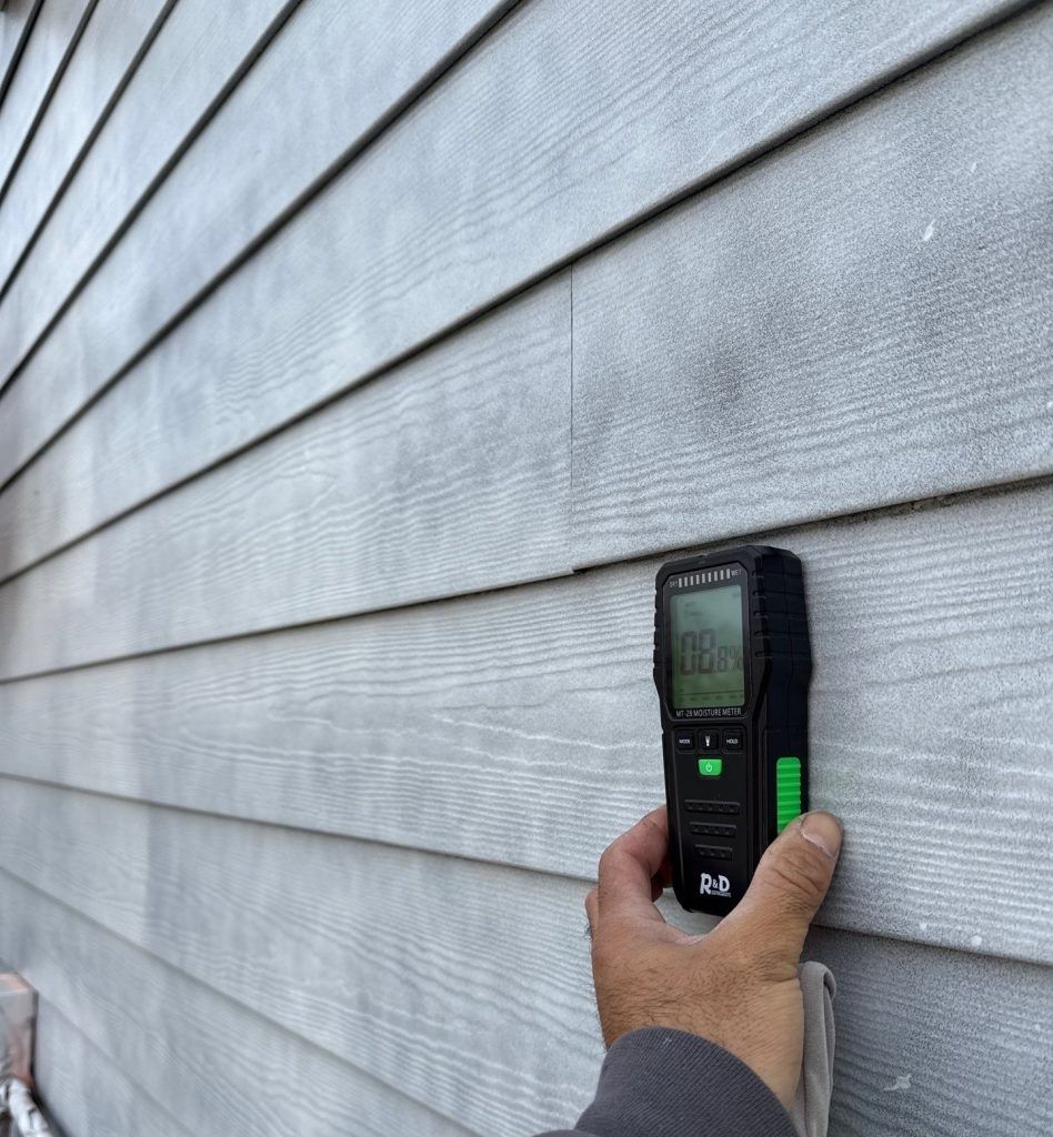 Hand holding a laser distance meter against gray house siding