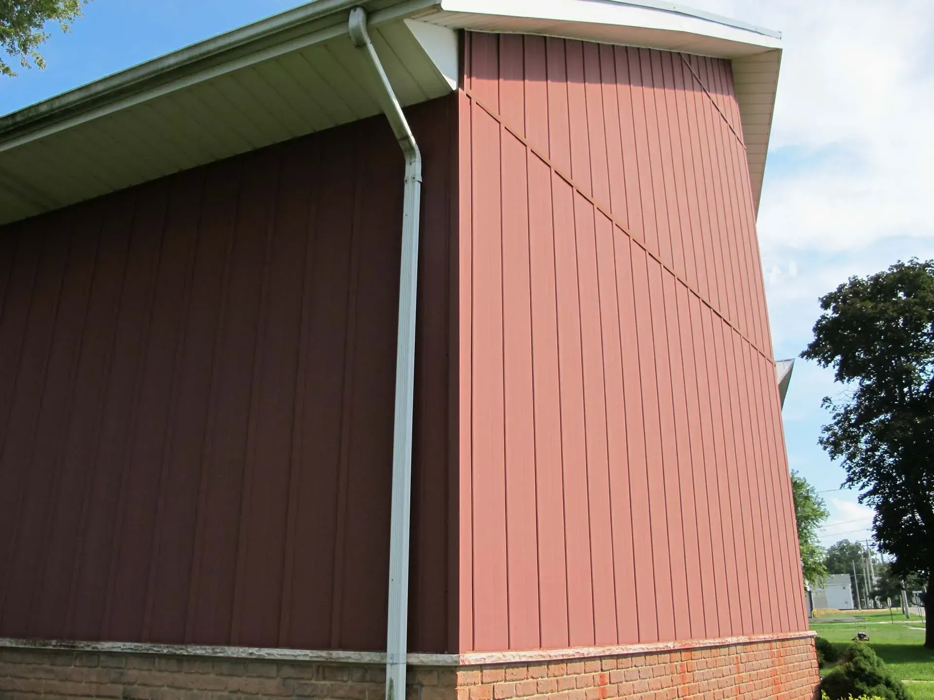 Red barn siding with a white roof overhang and gutter, shown from the corner in a grassy rural area.