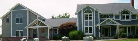 Two gray suburban houses with white trim and green roofs, viewed from the street.