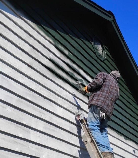 Person on a ladder painting the exterior siding of a house with a roller.