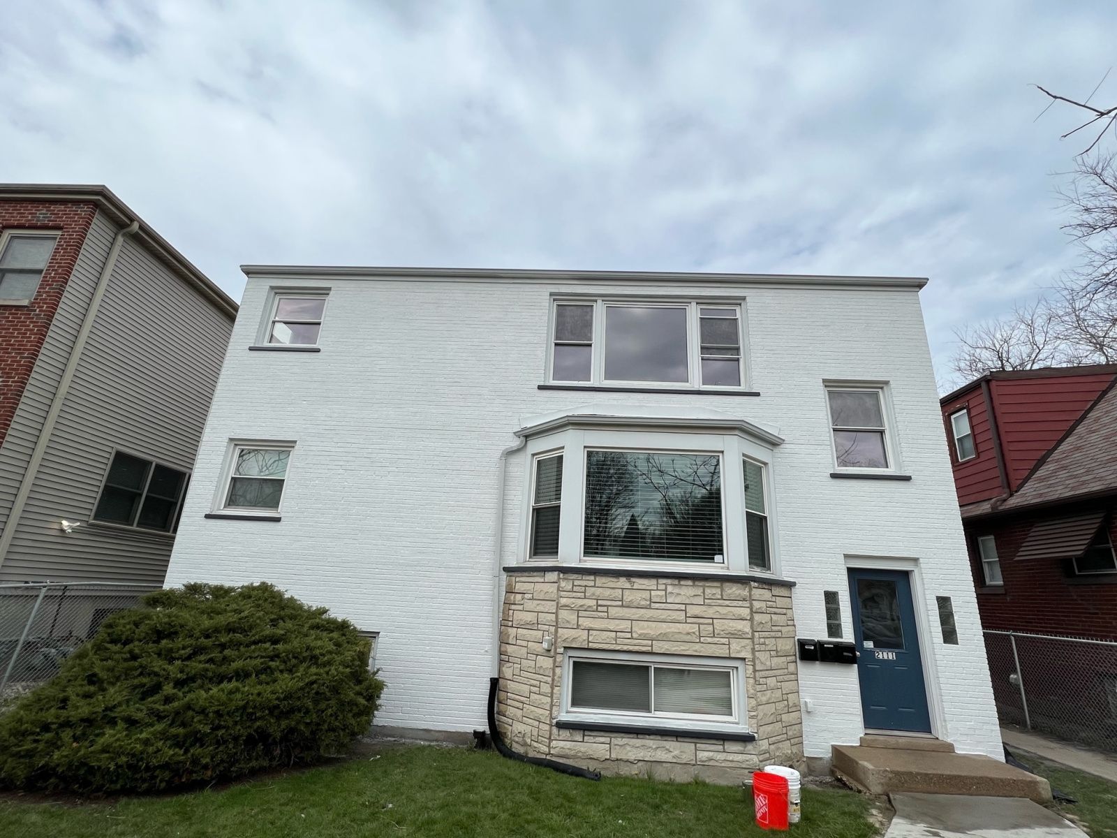 Two-story white house with stone bay window, blue front door, and red-roofed neighbors
