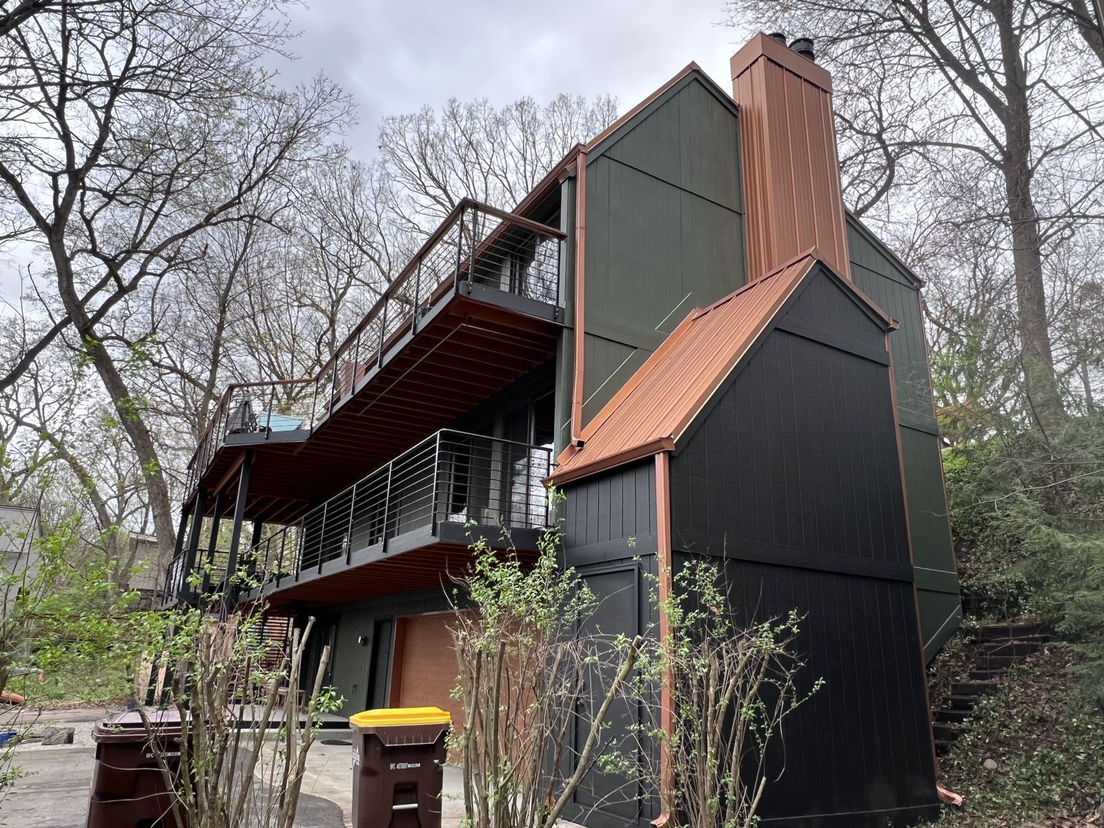 Modern black house with red roof and balconies in a wooded setting