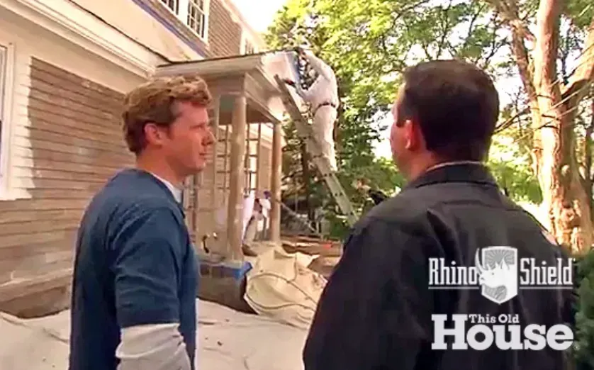 Two men standing outside a house, looking at each other in conversation.