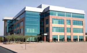 Modern glass-and-brick office building with teal windows and a wide paved plaza