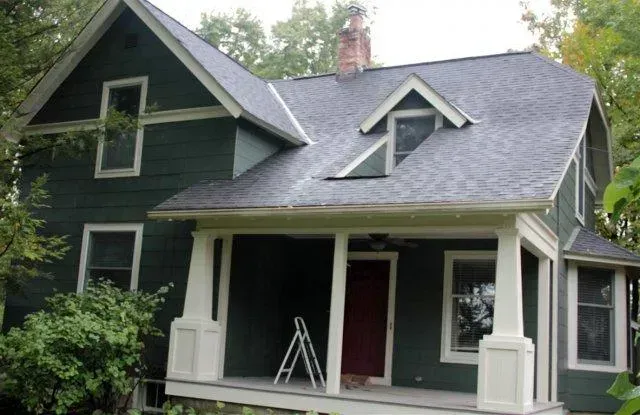 Dark green house with a porch, white trim, and a red front door under a gray roof.