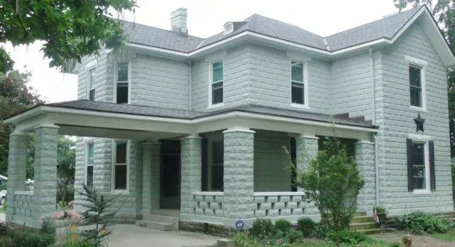 Light green two-story house with a covered porch and stone foundation
