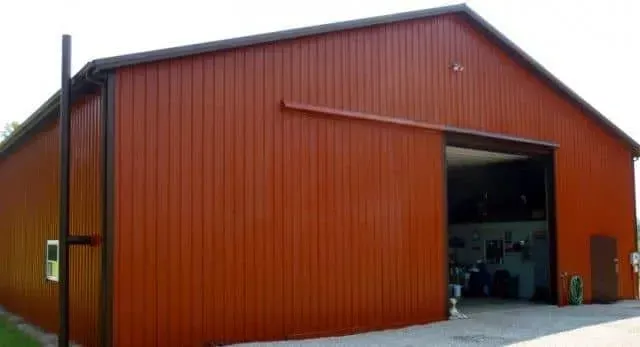 Red metal barn-style building with a large open garage door and black chimney pipe.