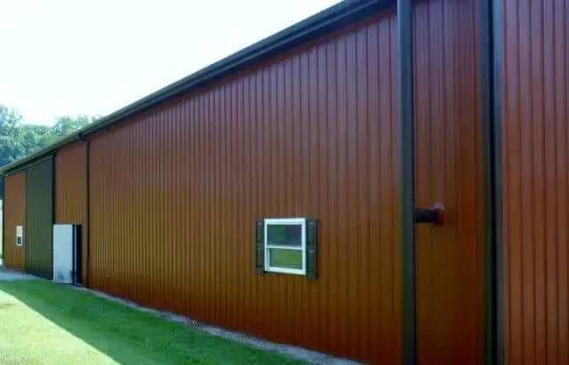 Brown metal building with a white door and small window beside a grassy lawn