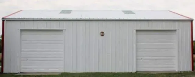 White metal garage with two roll-up doors and a central entrance on a grassy lot