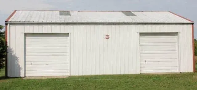 White metal garage with two roll-up doors on a grassy lot