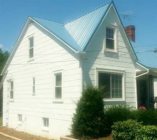 White two-story house with a blue metal roof and white trim, seen from the side in daylight.