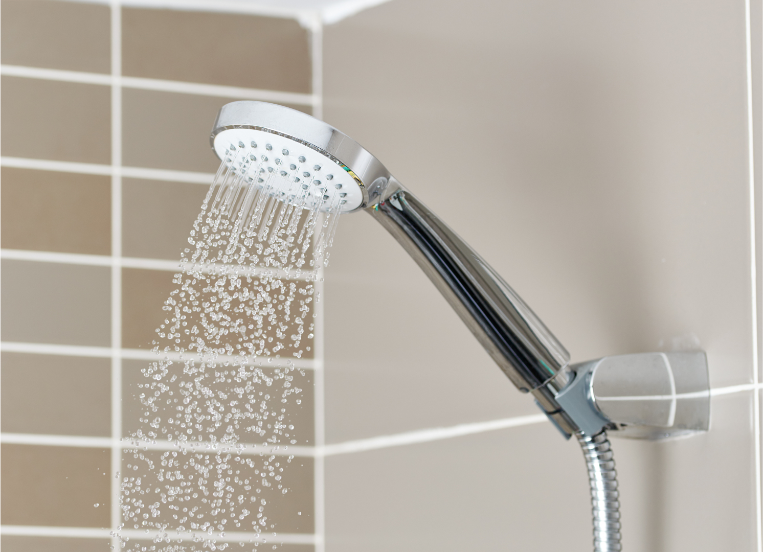 Chrome showerhead spraying water in a tiled bathroom.