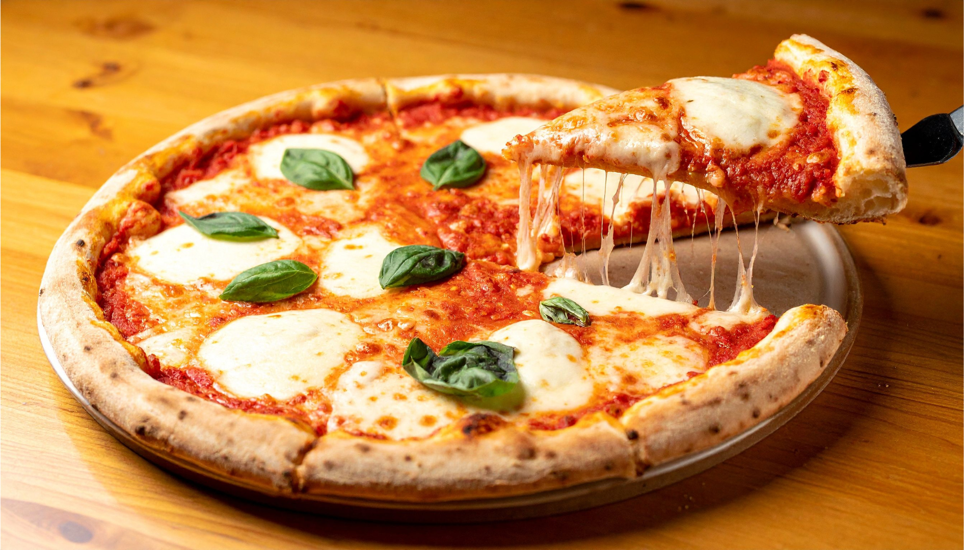 Pizza with mozzarella, basil, and tomato sauce; slice being lifted, cheese stretching.