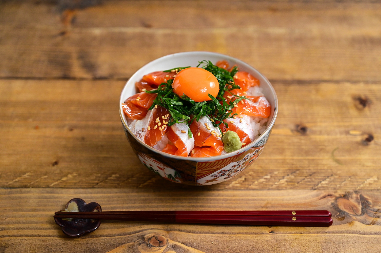 Bowl of salmon and rice topped with egg yolk and herbs, chopsticks.