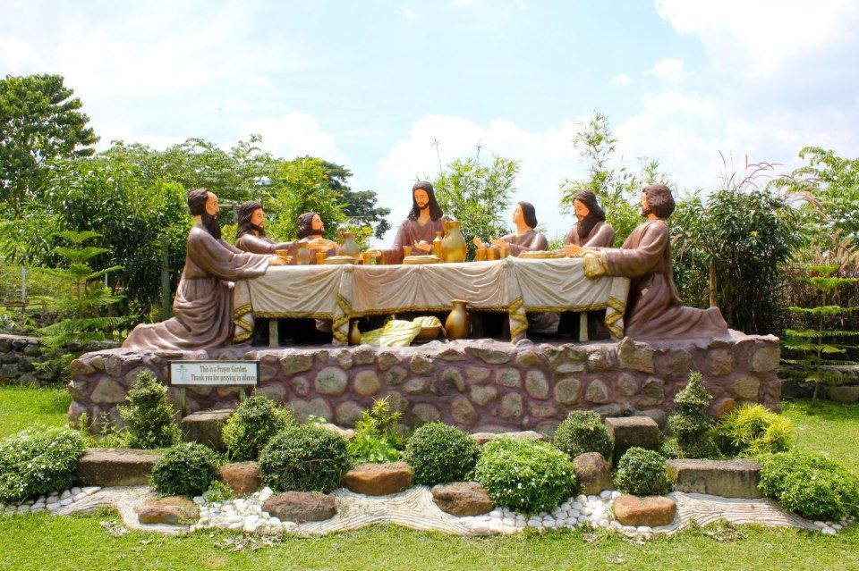 Statues depicting Jesus and disciples at the Last Supper, set outdoors with greenery and sky.