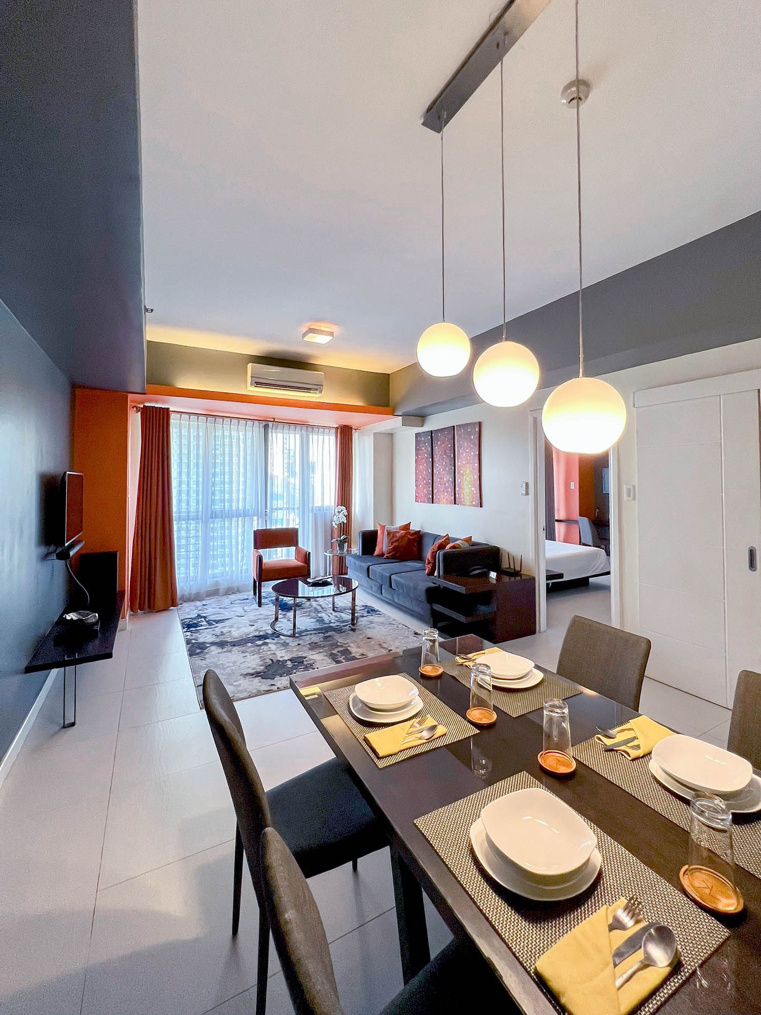 Dining area with table set for six, leading to a living room with sofa, chair, and open doorway to bedroom.